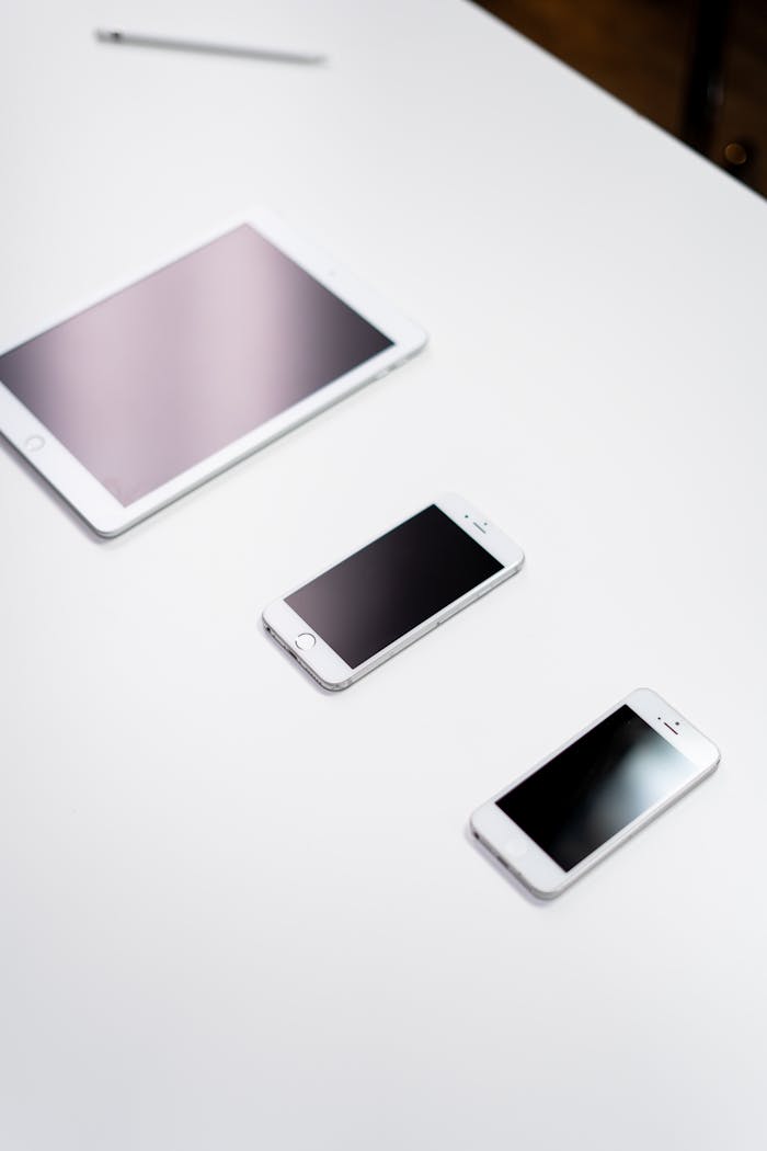 Overhead view of a digital tablet, smartphone, and stylus on a white surface.